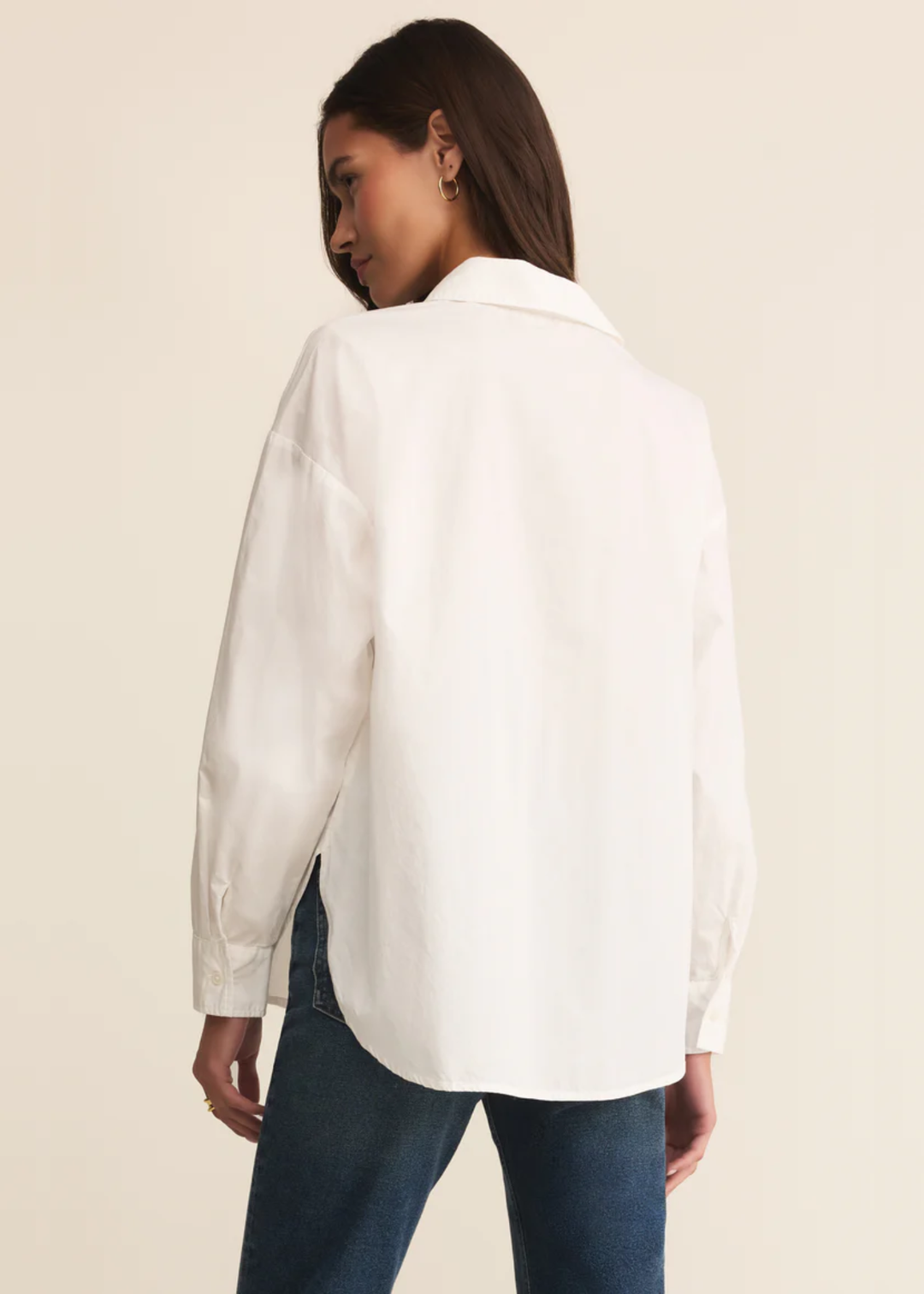 Woman turned to the side wearing a white button down shirt with jeans