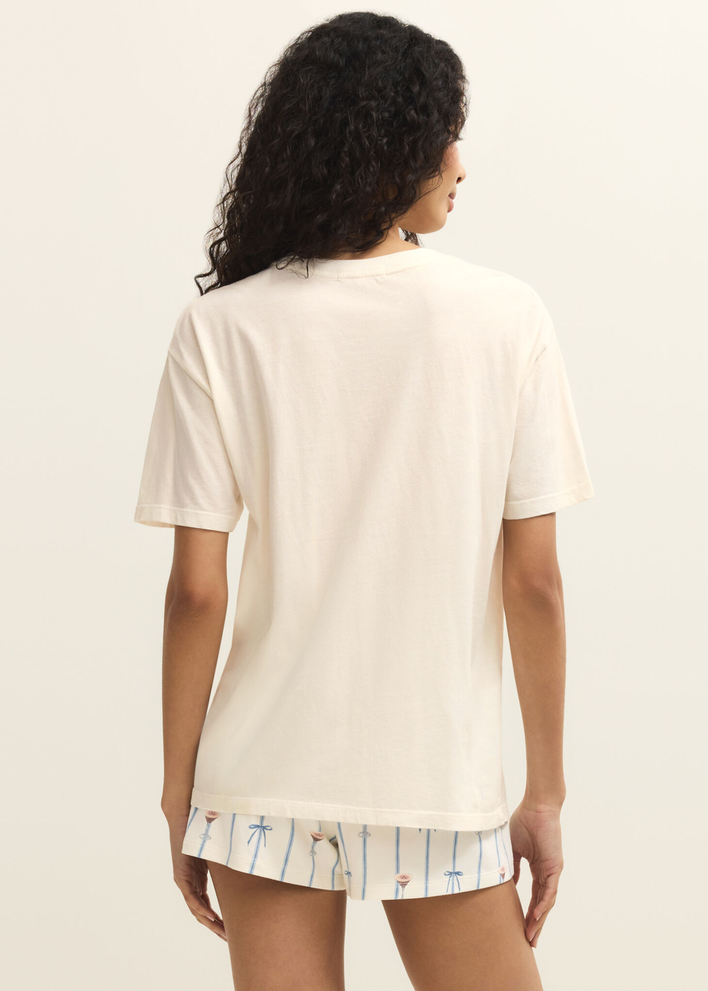 Woman turned around wearing a white shirt and shorts against a white background