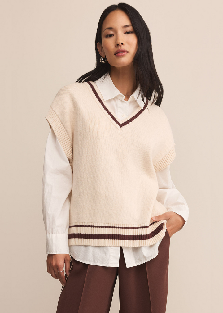 Woman wearing a cream sweater vest with brown stripe trim over a white button down