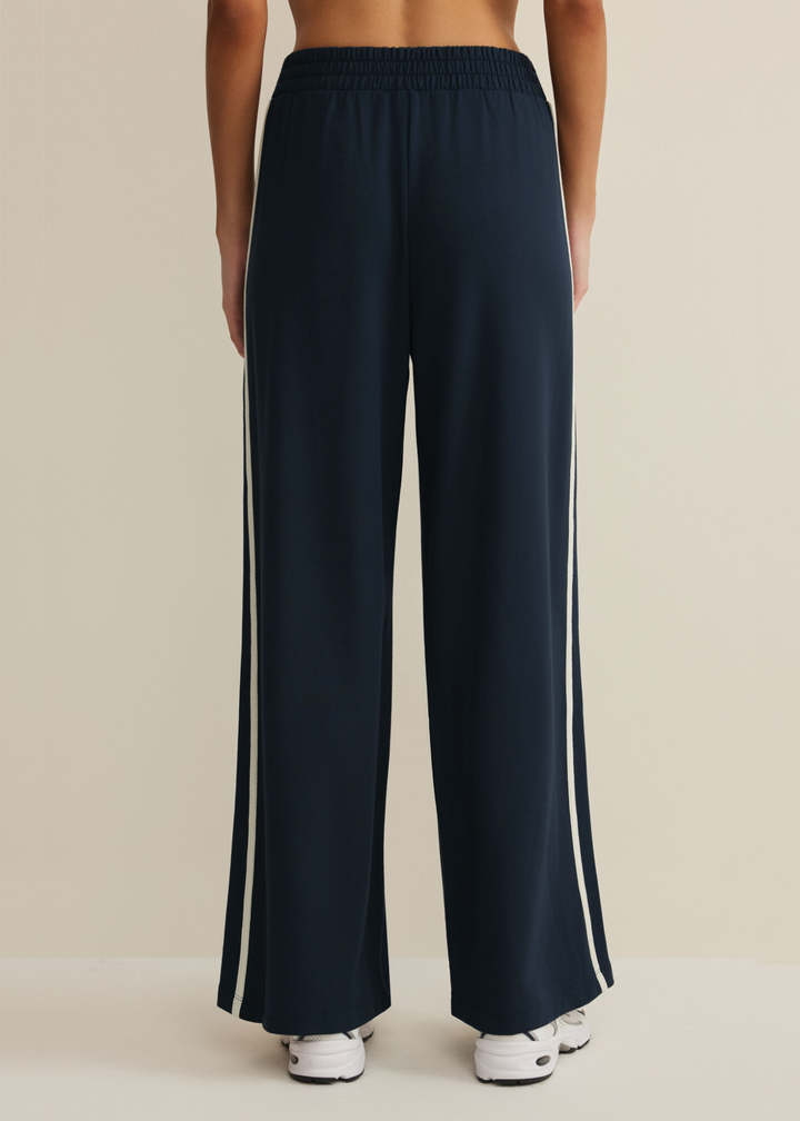 Woman turned around wearing navy sweatpants with white side stripes against a white background