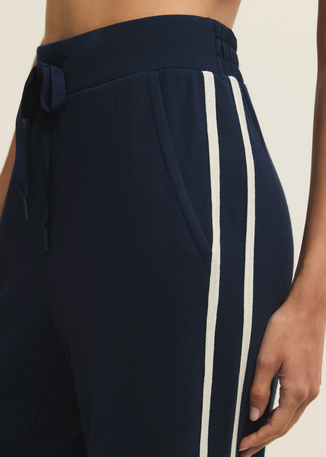Close up of a woman wearing navy sweatpants with white side stripes against a white background