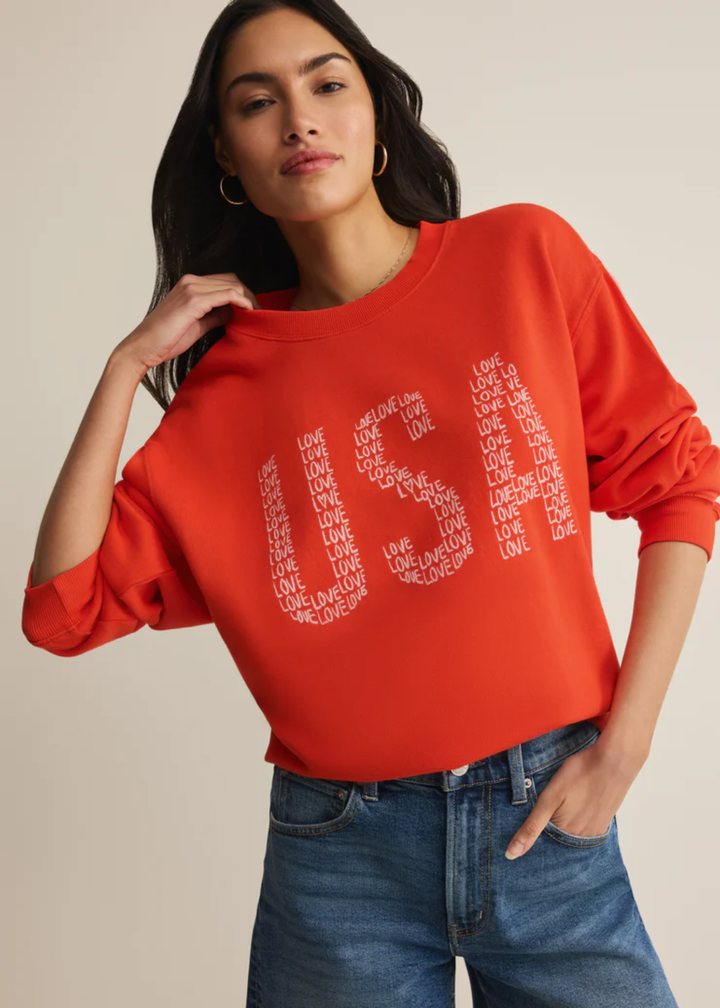 Woman wearing a red sweatshirt with a "USA" graphic and "love" lettering with denim shorts