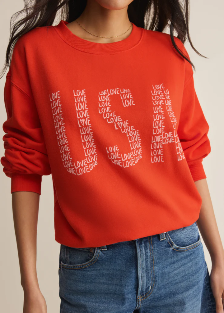 Woman wearing a red sweatshirt with a "USA" graphic and "love" lettering with denim shorts