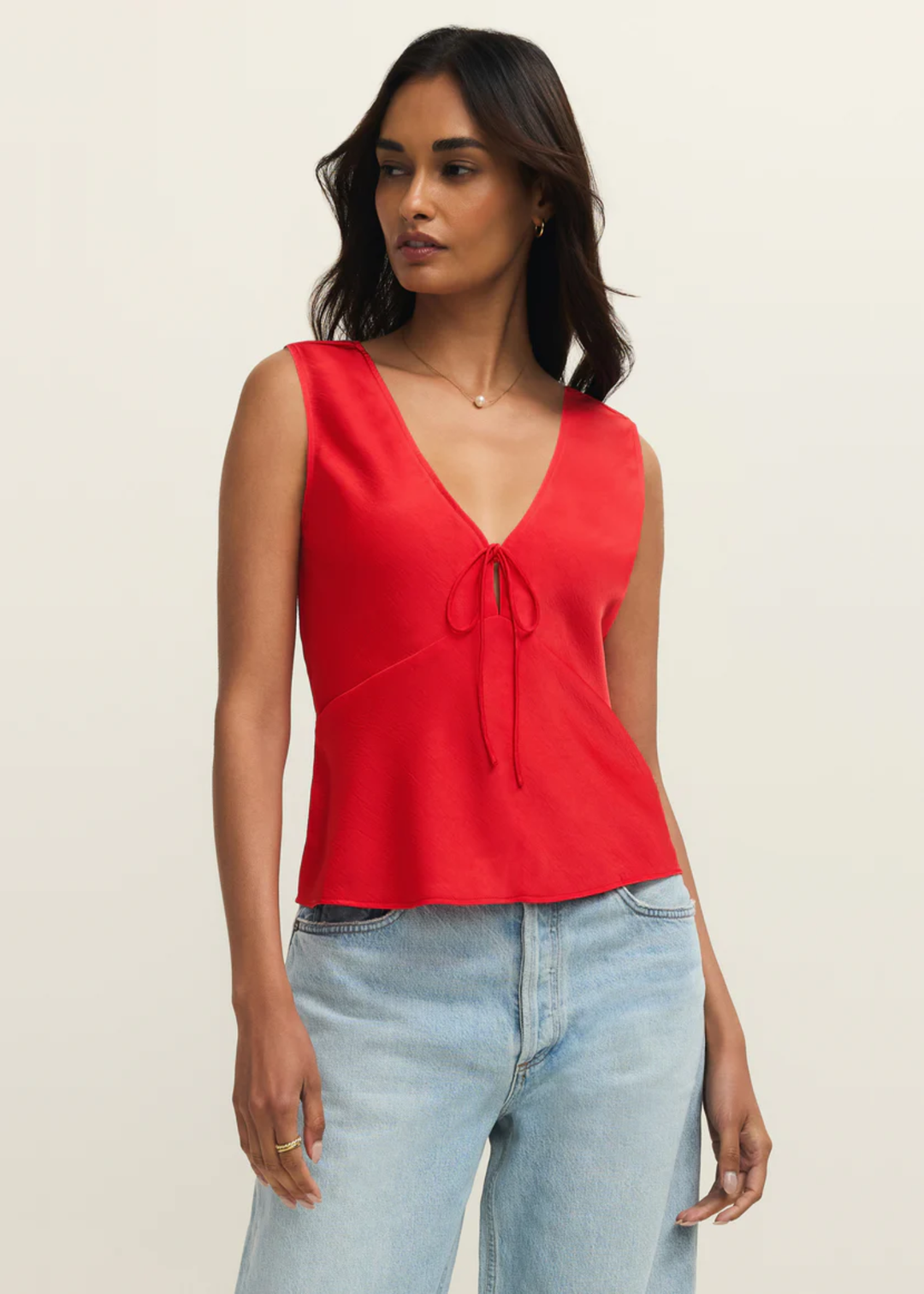 Woman wearing a red satin tank top with a front bow tie and jeans against a white background