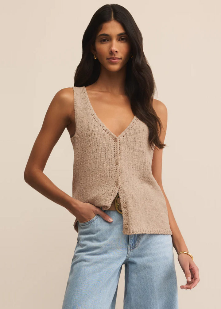 Woman wearing a tan button up sweater vest with blue jeans