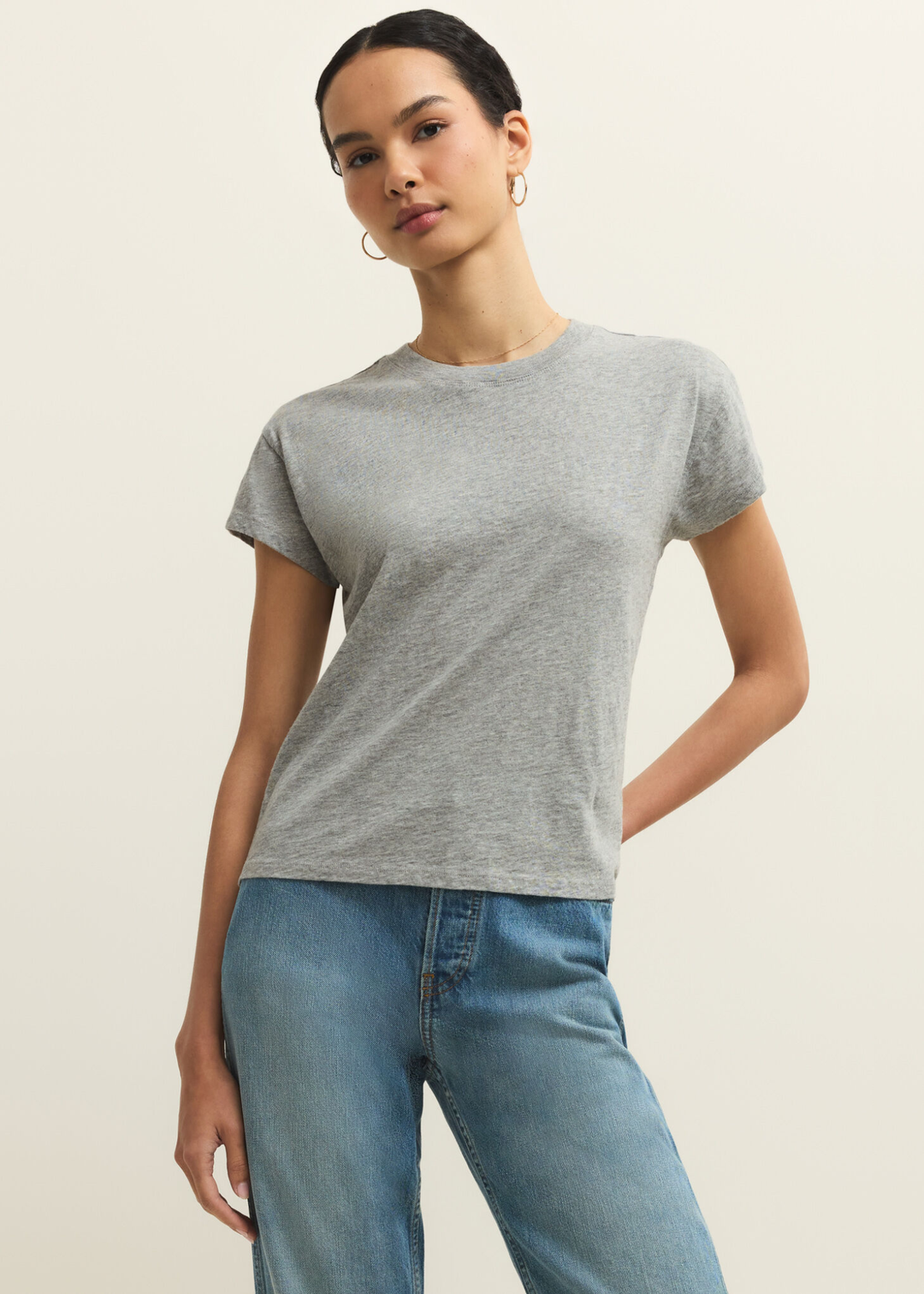 Woman wearing a grey short sleeve t-shirt and jeans against a grey background