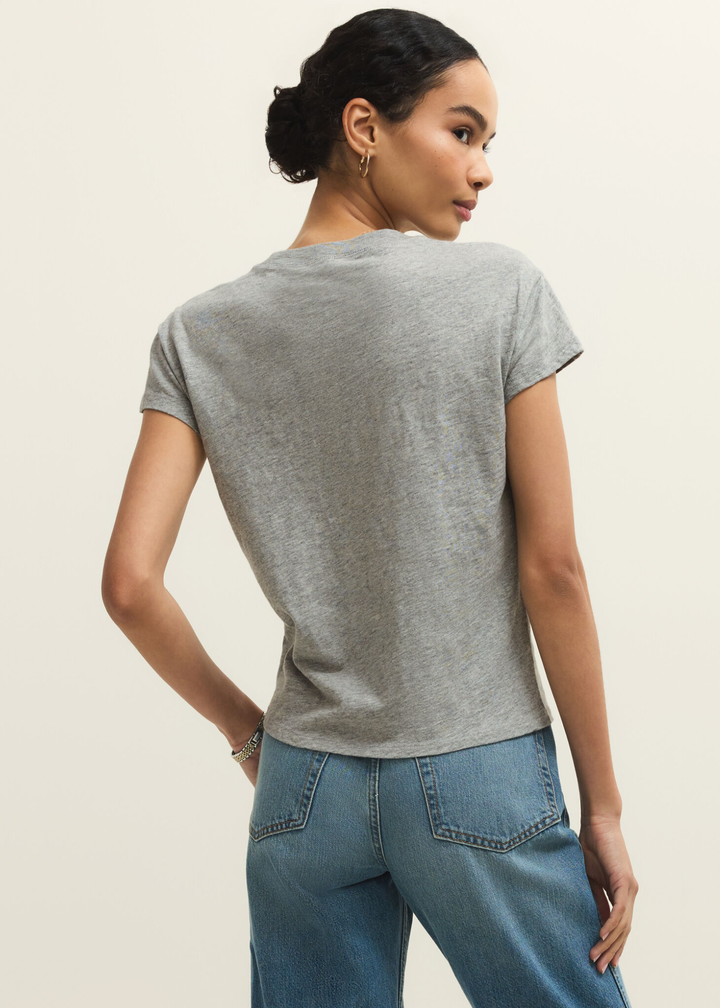 Woman turned around wearing a grey short sleeve t-shirt and jeans against a grey background