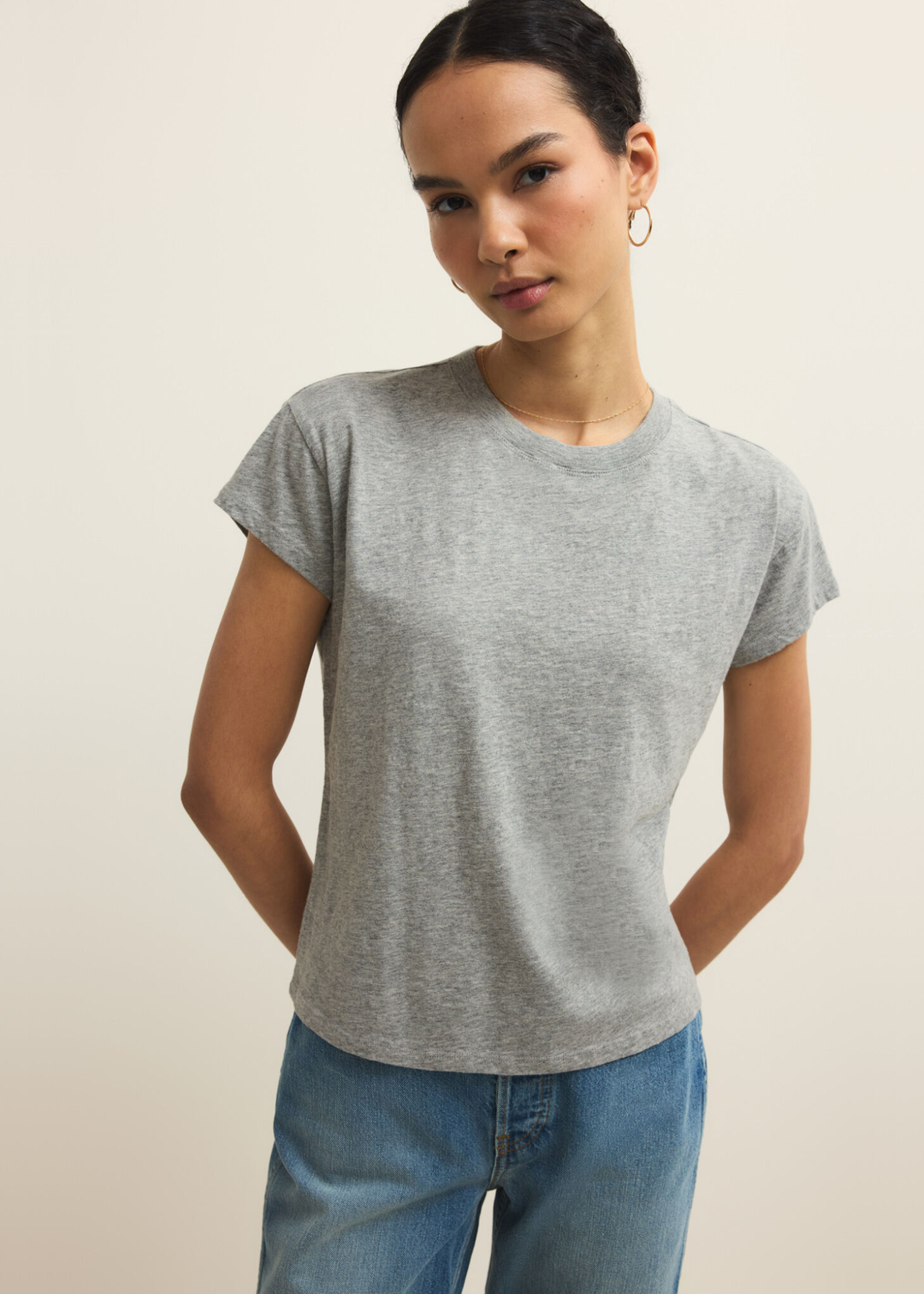 Woman wearing a grey short sleeve t-shirt and jeans against a grey background