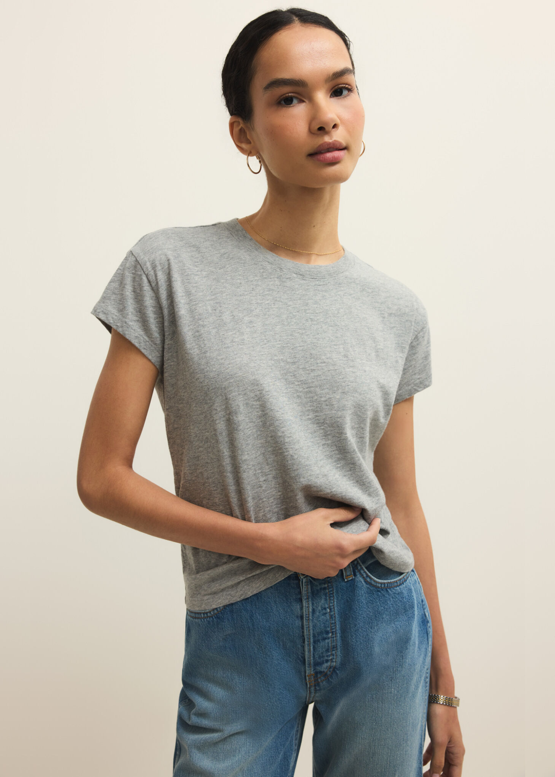 Woman wearing a grey short sleeve t-shirt and jeans against a grey background