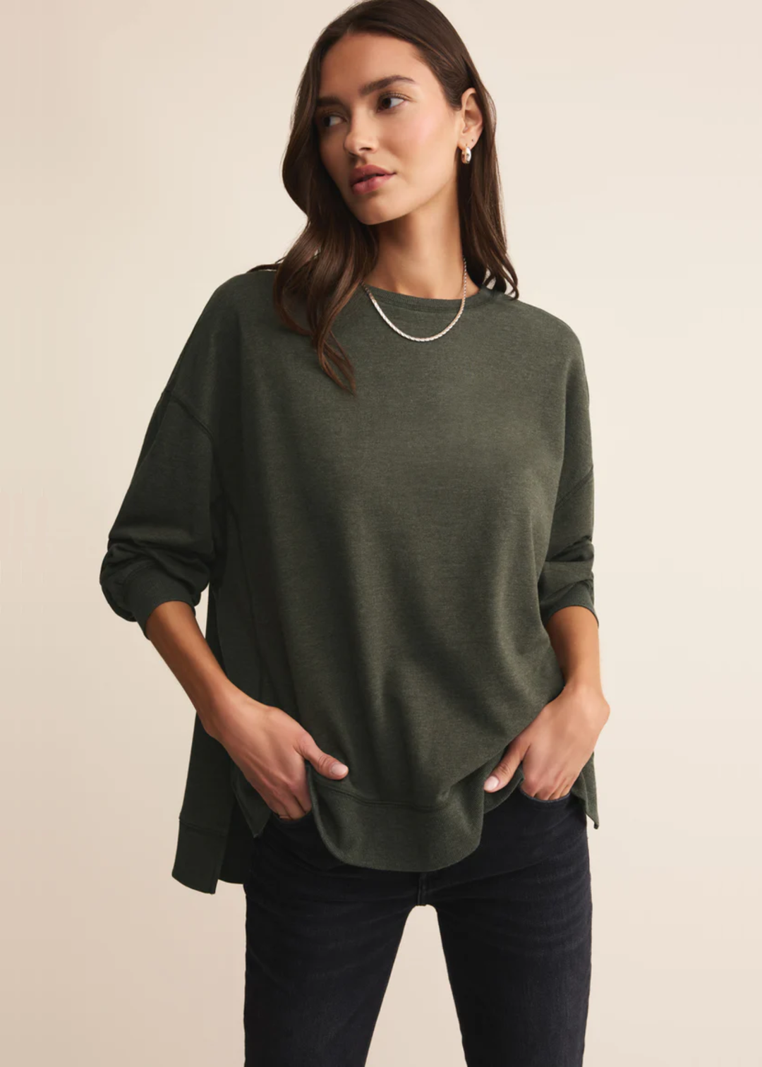 Woman wearing a dark green sweatshirt with black pants standing in front of a white background