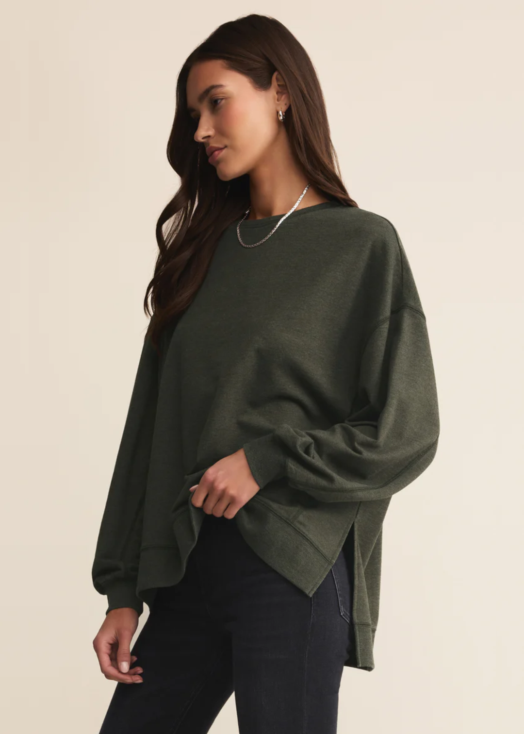 Woman wearing a dark green sweatshirt with black pants standing in front of a white background