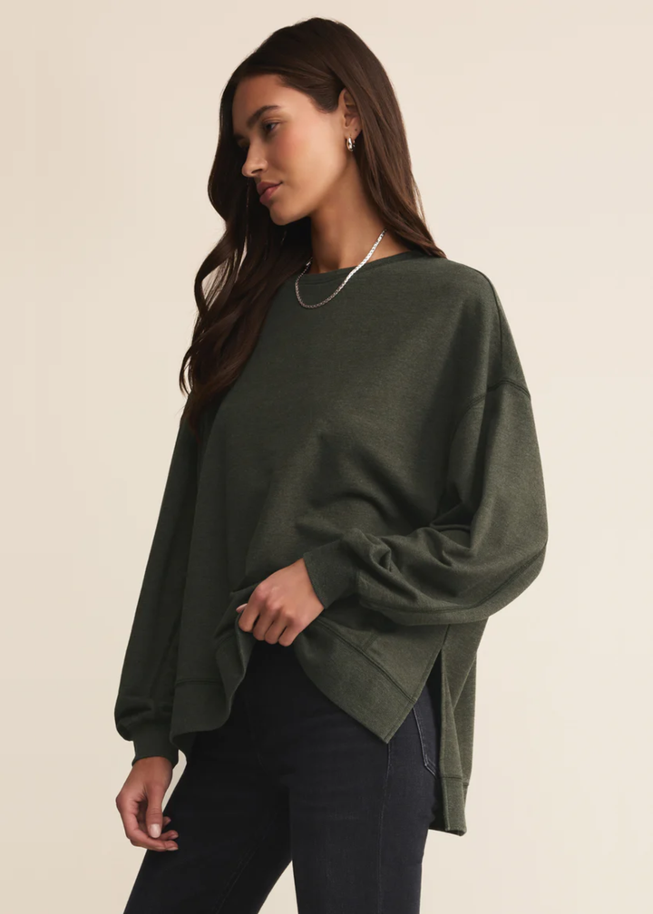Woman wearing a dark green sweatshirt with black pants standing in front of a white background
