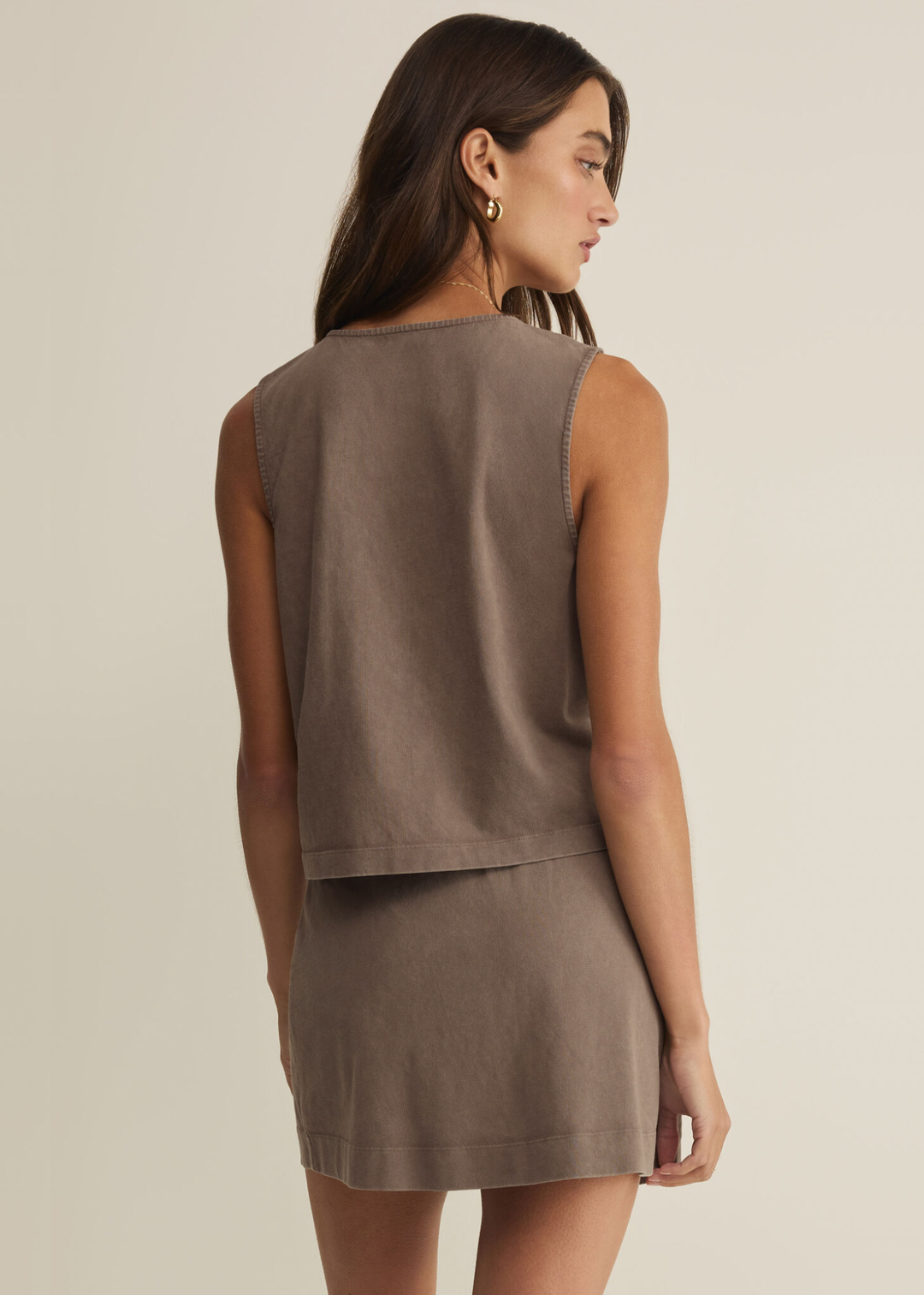 Woman turned around wearing a taupe button up tank top with a matching skirt