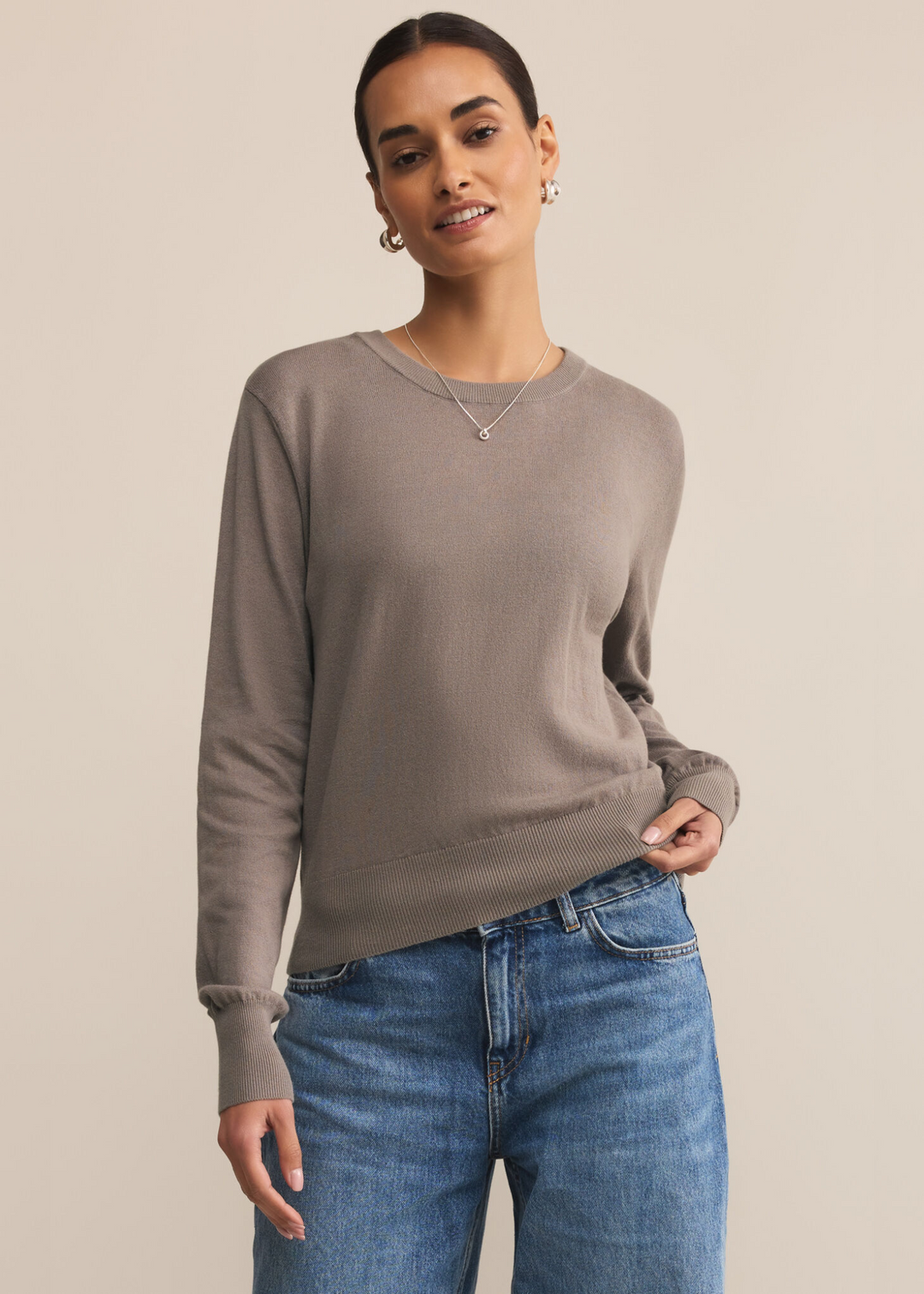 Woman wearing a grey sweater with jeans in front of a grey background