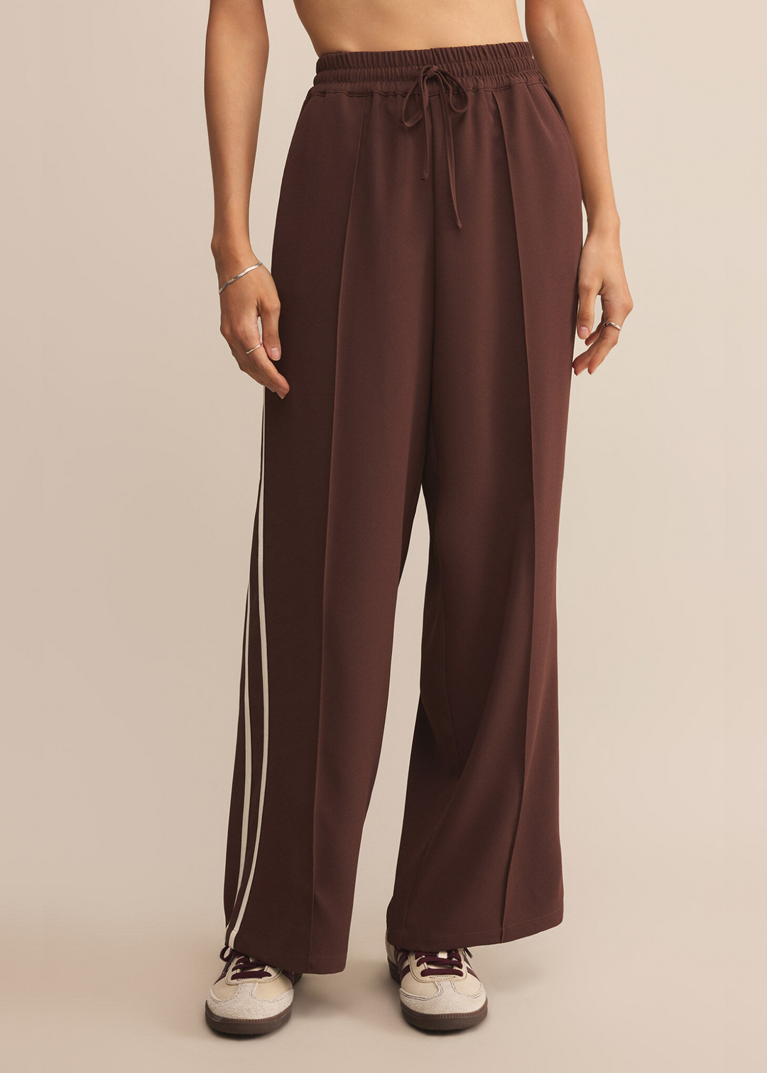 Woman wearing brown wide leg pants with white side stripes and an elastic waistband