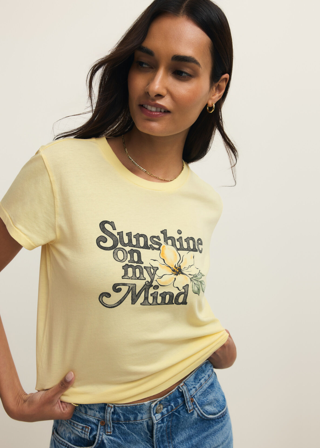 Woman wearing a yellow t-shirt with a "Sunshine on my Mind" graphic and jeans against a grey background