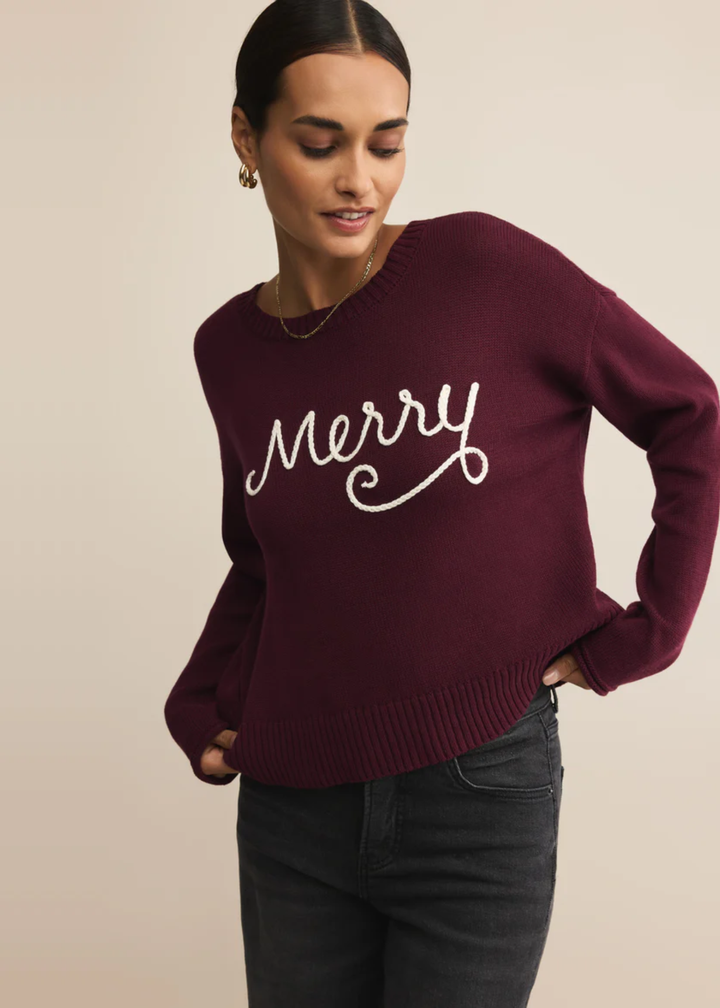Woman wearing a maroon sweater with white "Merry" lettering in front of a tan background