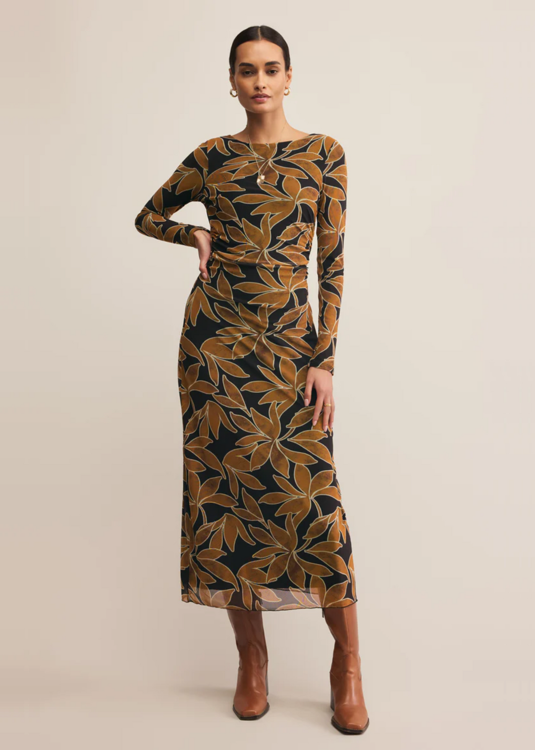 Woman wearing a black midi dress with a brown floral print in front of a grey background