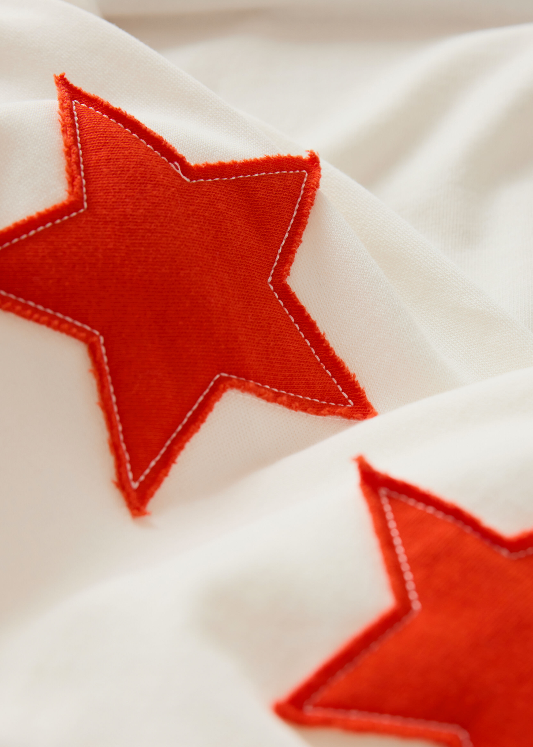 Close up of a cream sweatshirt with red stars stitched on the sleeve