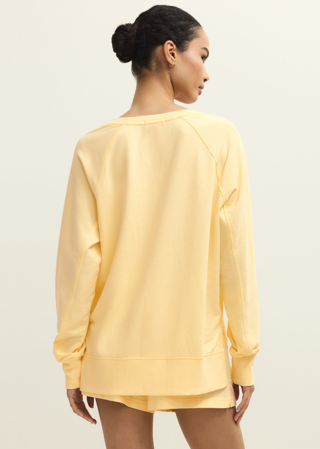 Woman turned around wearing a yellow v-neck sweatshirt with yellow shorts