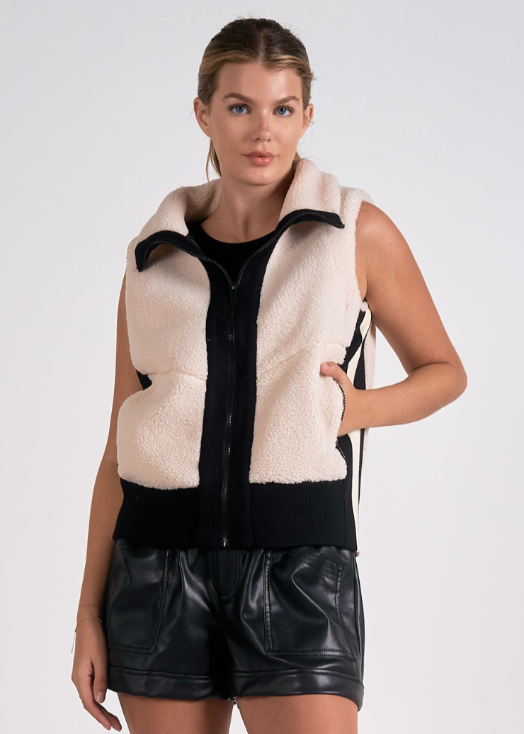 A women's sherpa vest in cream and black, featuring a zip-up front and cozy design, perfect for layering.