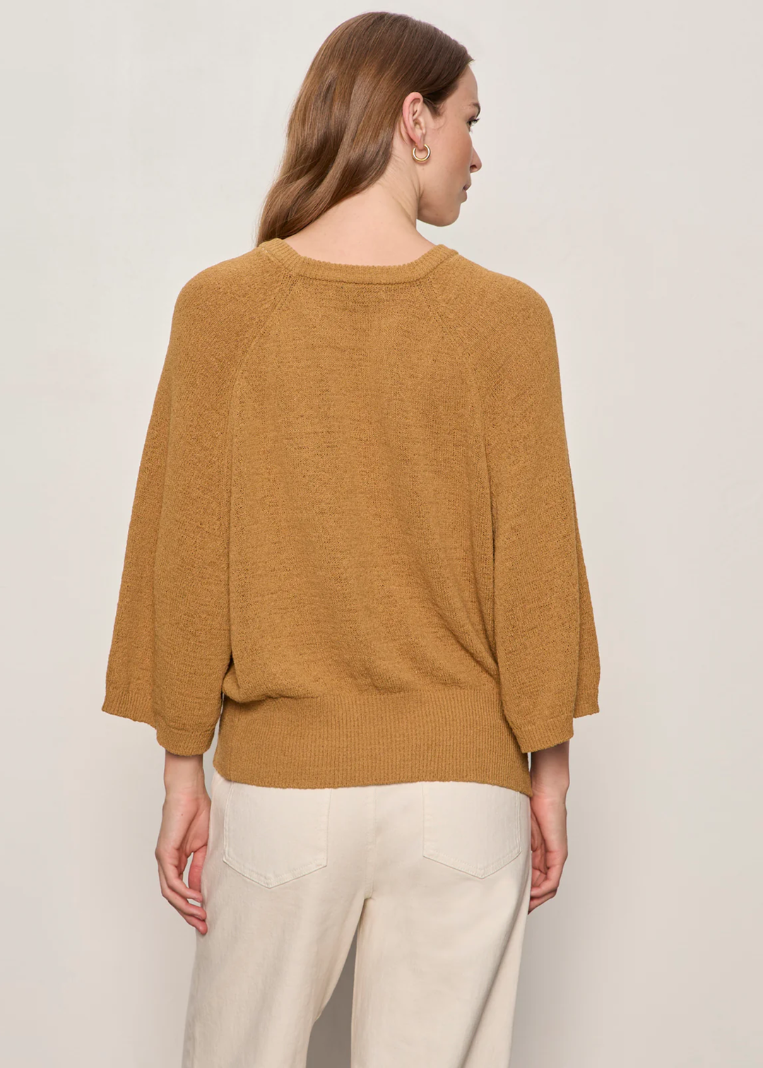 Woman wearing rust sweater with 3/4 length sleeves and is turned around. 