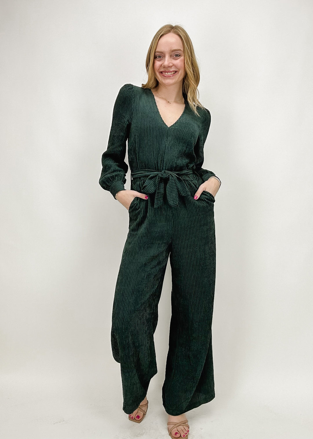 A woman wearing a dark green ribbed V-neck jumpsuit with long sleeves, wide legs, and a drawstring waist, styled for a chic and comfortable look.