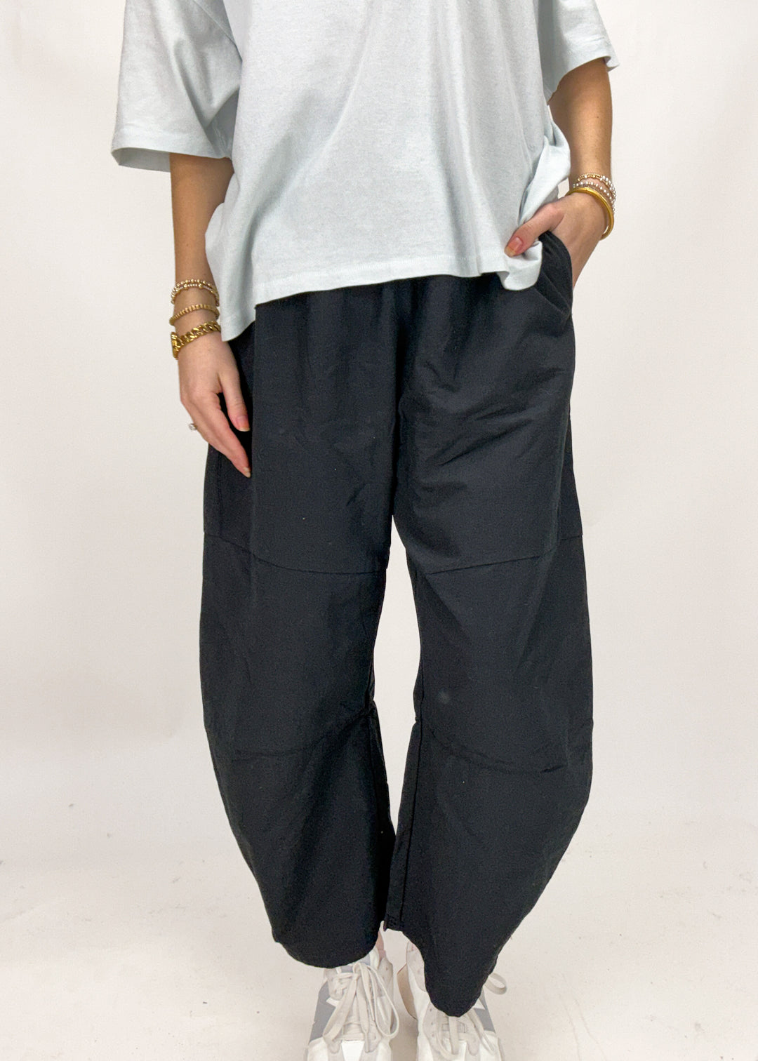Person wearing black barrel pants and a white shirt on a plain background