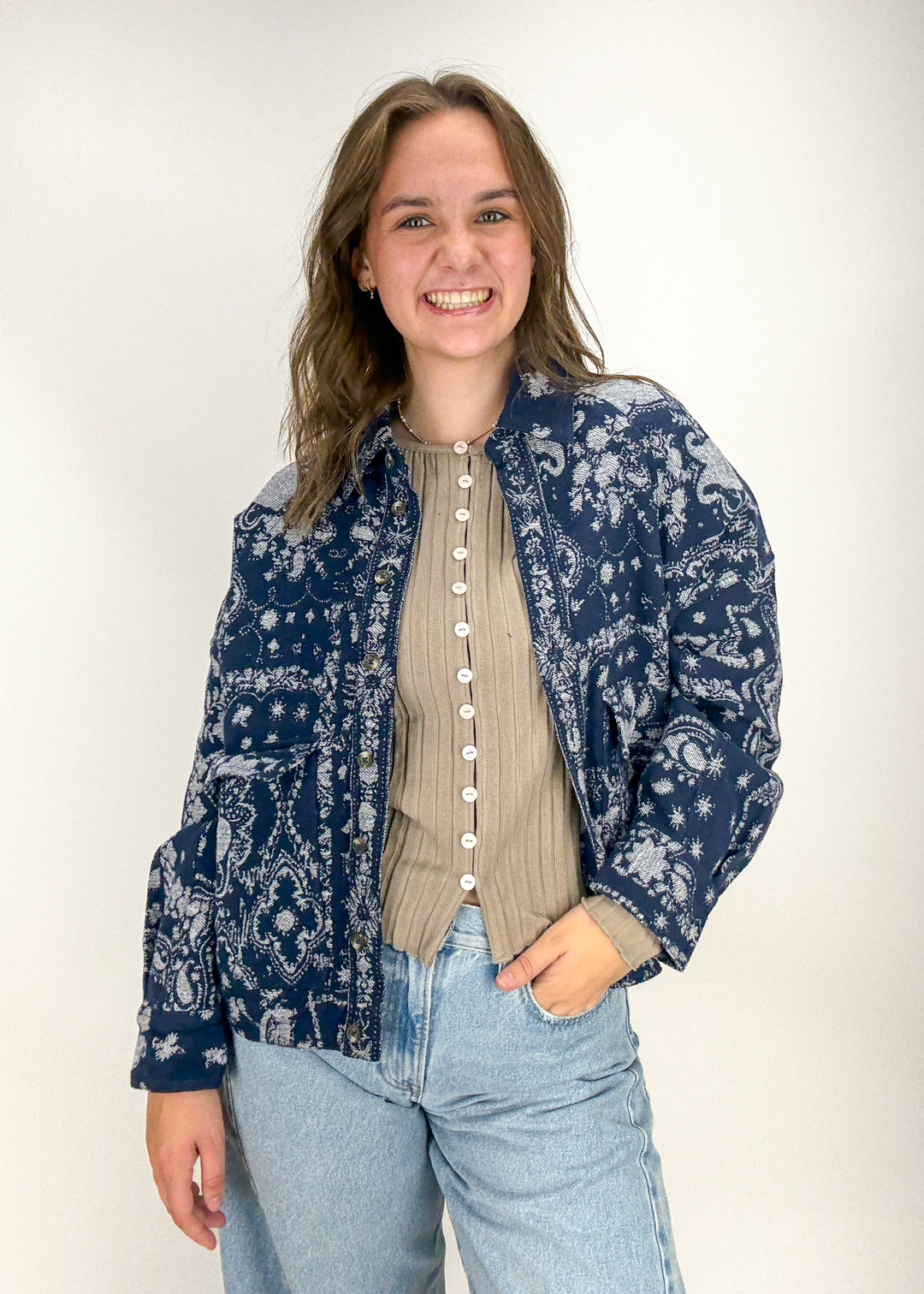 Woman wearing a blue patterned shirt over a beige cardigan and light blue jeans 