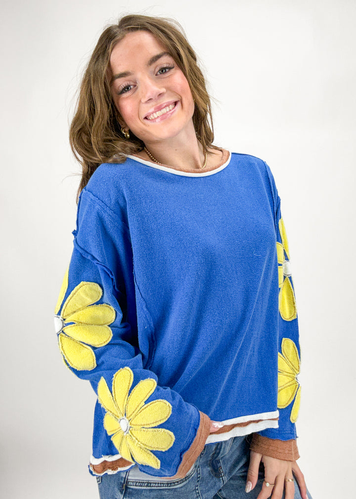 Woman wearing a blue sweater with yellow floral patterns on a white background