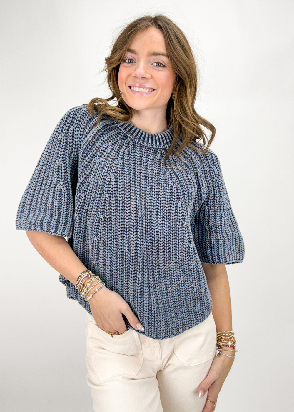 Woman wearing a blue knitted sweater and beige pants on a white background