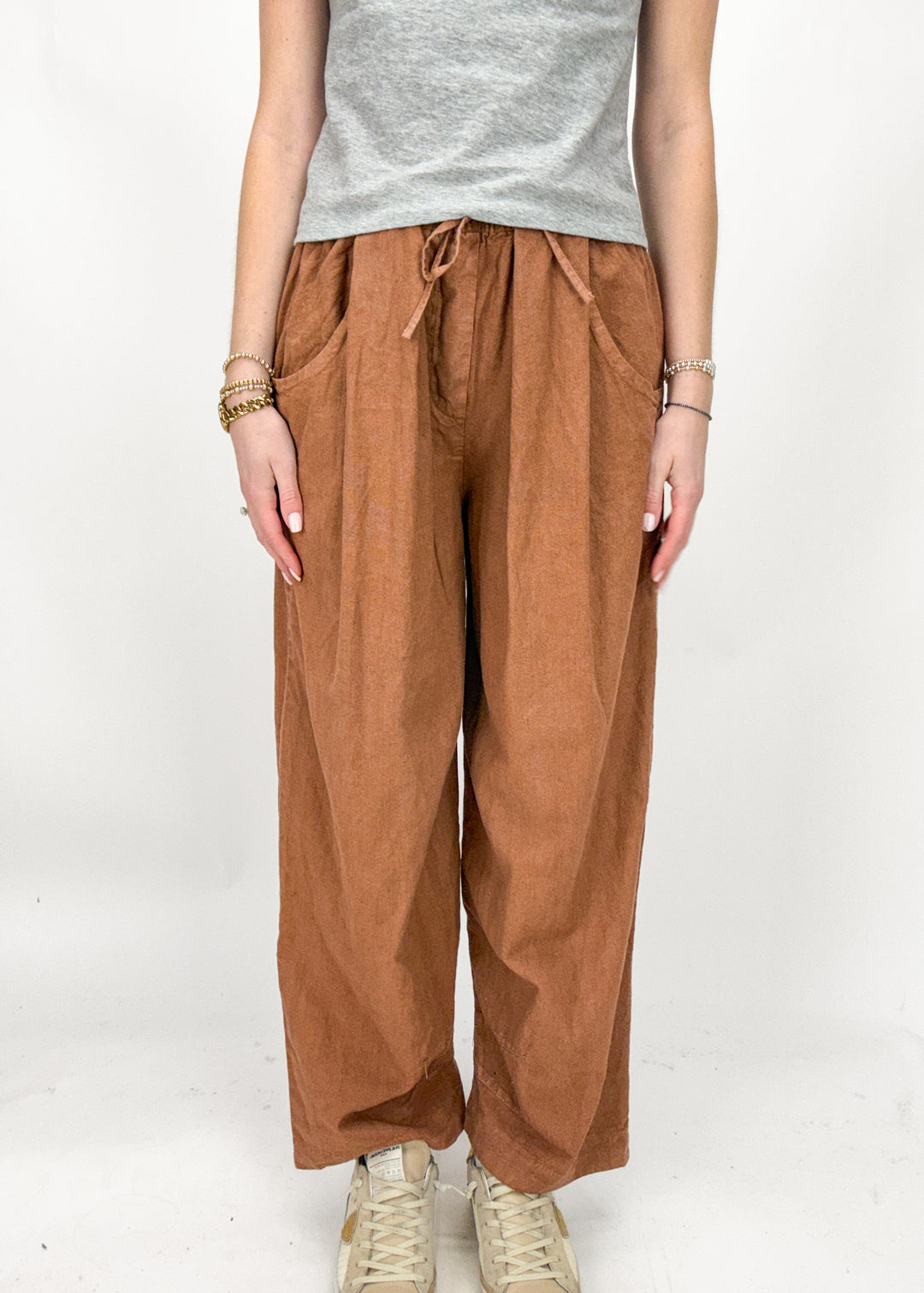 Person wearing rust wide-leg pants and a gray top on a white background