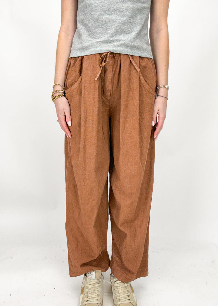 Person wearing rust wide-leg pants and a gray top on a white background