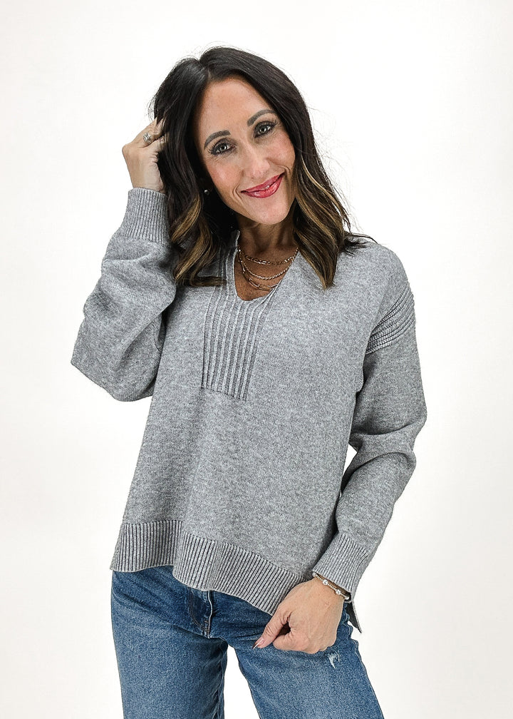 A cozy grey V-neck sweater featuring ribbed detailing along the neckline, sleeves, and hem, perfect for a casual and stylish look.