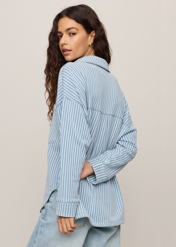 Woman wearing denim with white striped button down, turned around looking over her shoulder. 