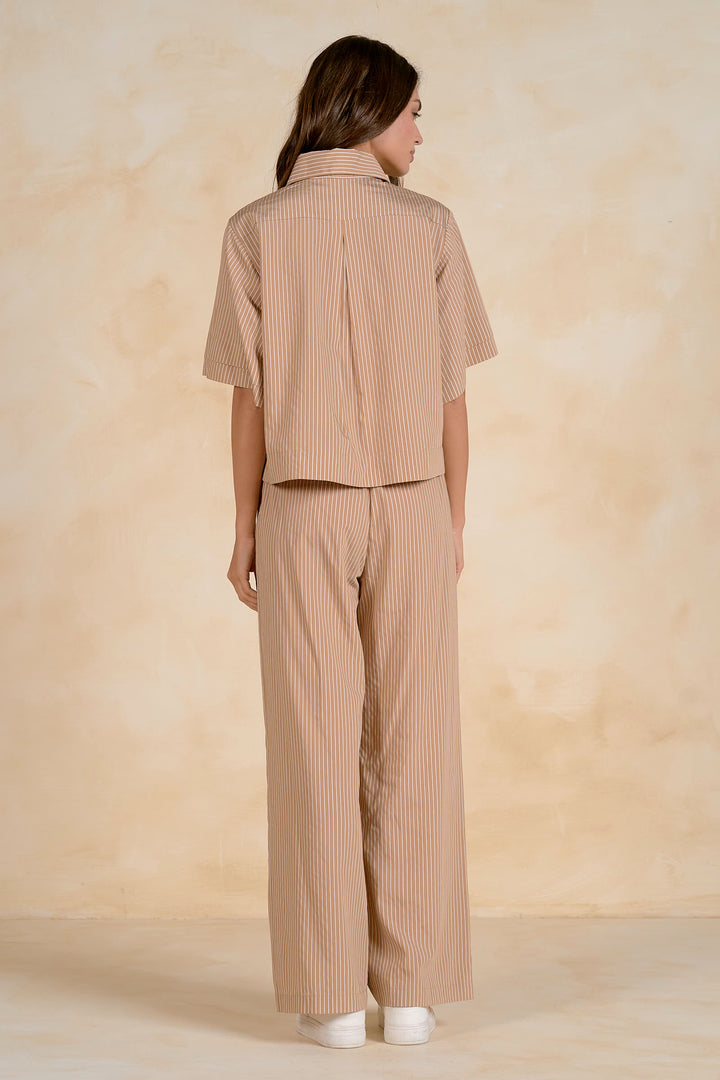 Woman wearing a beige striped shirt and pants against a beige background