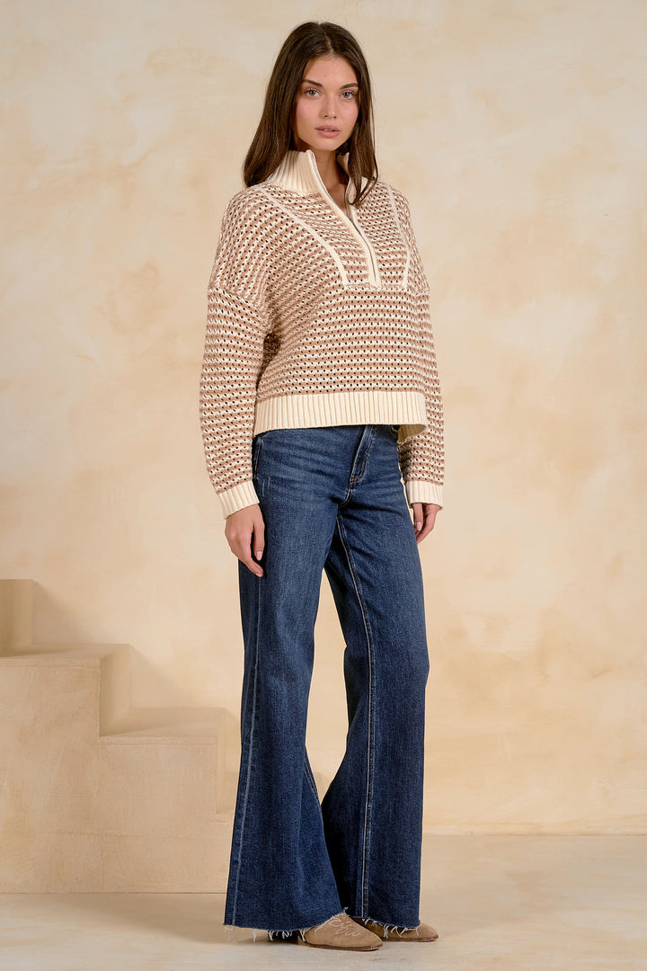 Woman wearing a patterned sweater and blue jeans against a beige background