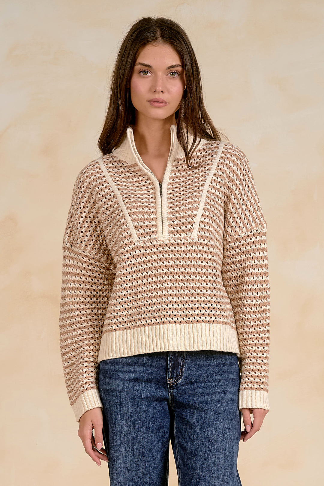 Woman wearing a beige knitted sweater with a white zipper against a beige background