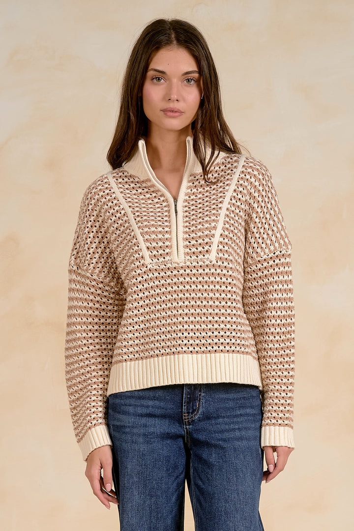 Woman wearing a beige knitted sweater with a white zipper against a beige background
