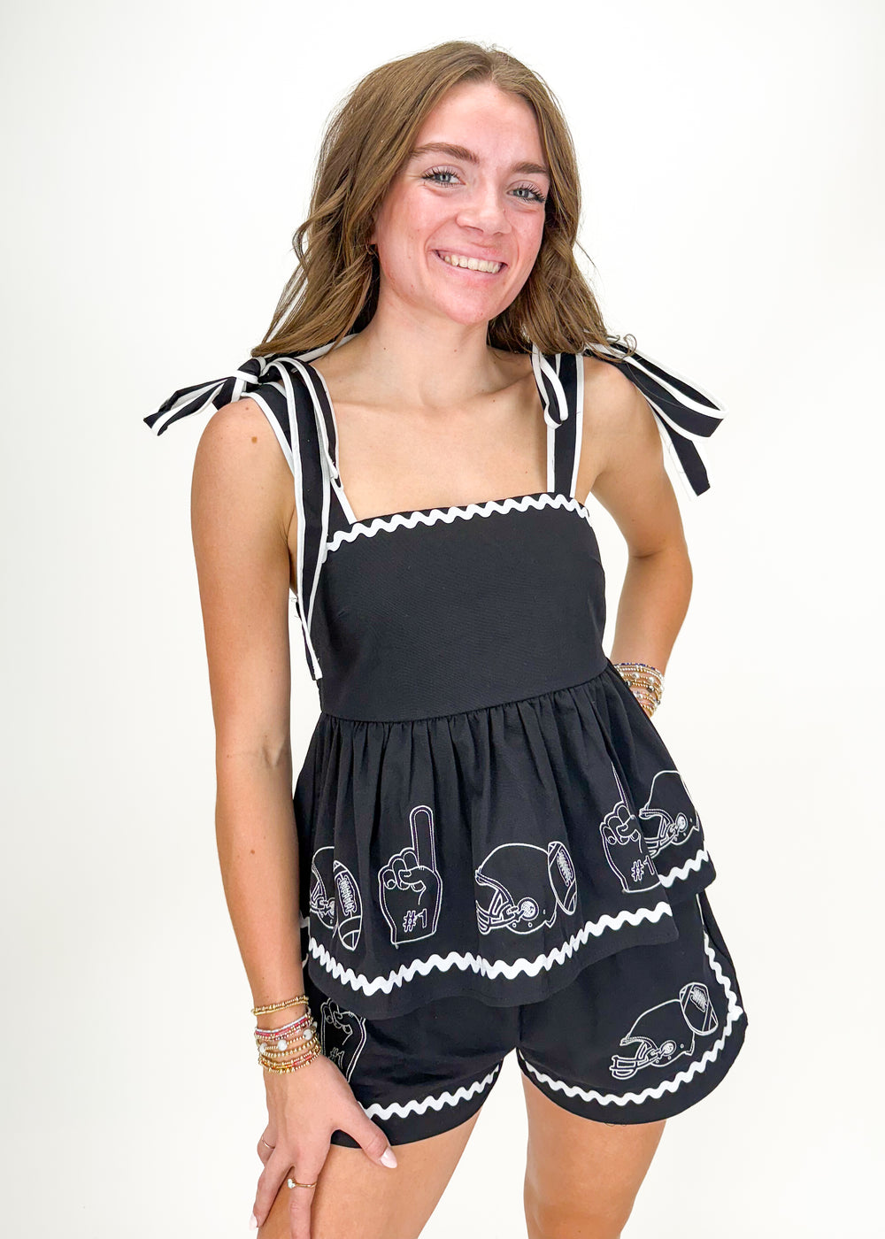 woman wearing black tank top and short set with white embroidered footballs, helmets, and foam fingers, wavy trim details, and tie straps