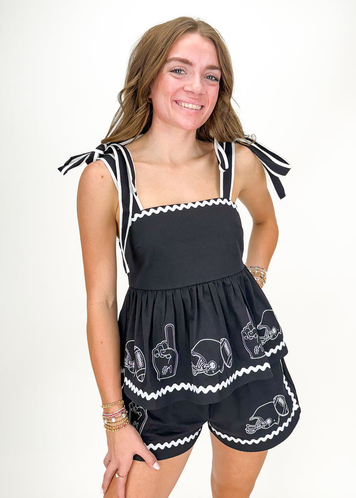 woman wearing black tank top and short set with white embroidered footballs, helmets, and foam fingers, wavy trim details, and tie straps