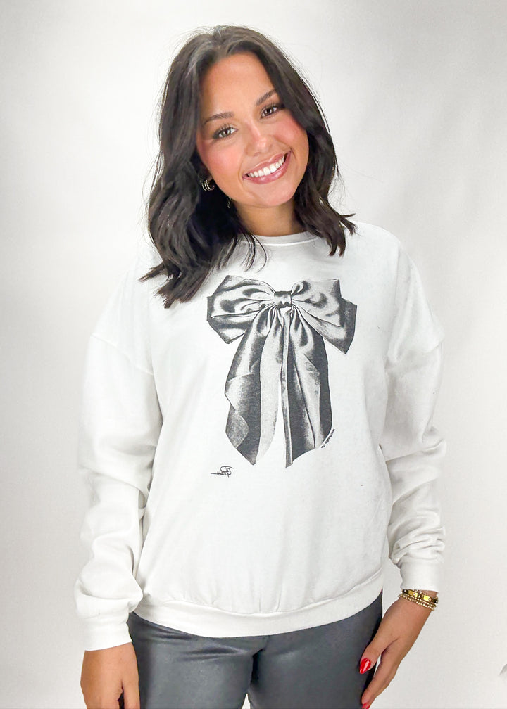 Woman wearing a white sweatshirt with a black bow design on a plain background