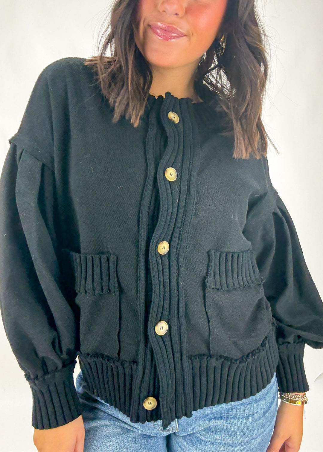 Person wearing a black cardigan with gold buttons on a plain background