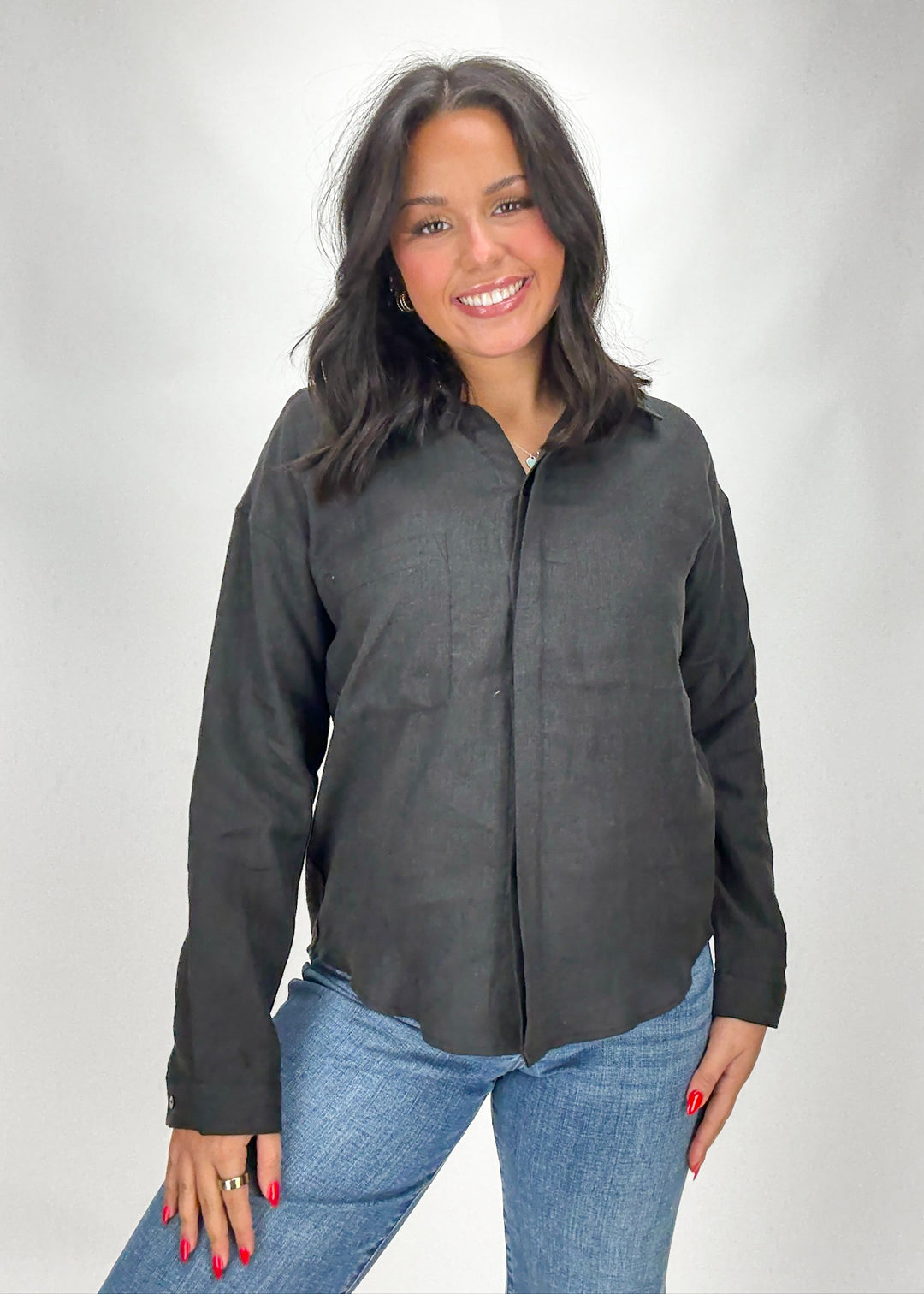 Woman wearing a dark gray button-up shirt and blue jeans on a white background
