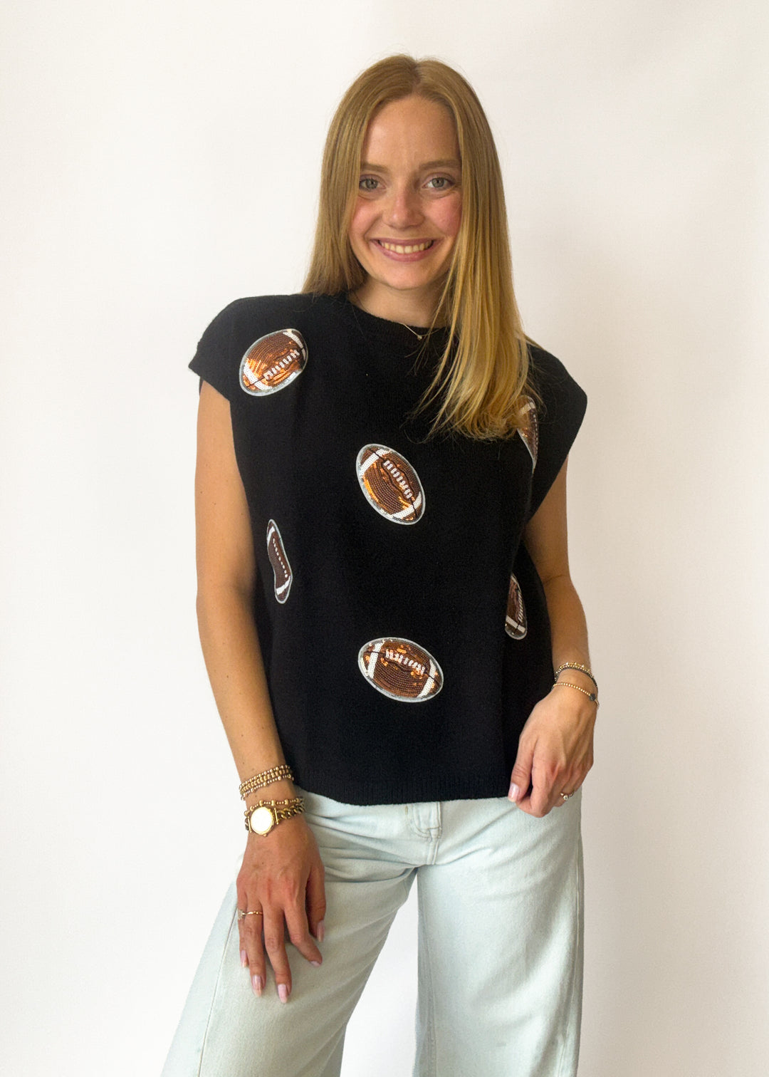 Woman wearing a black sleeveless top with football patches on a white background