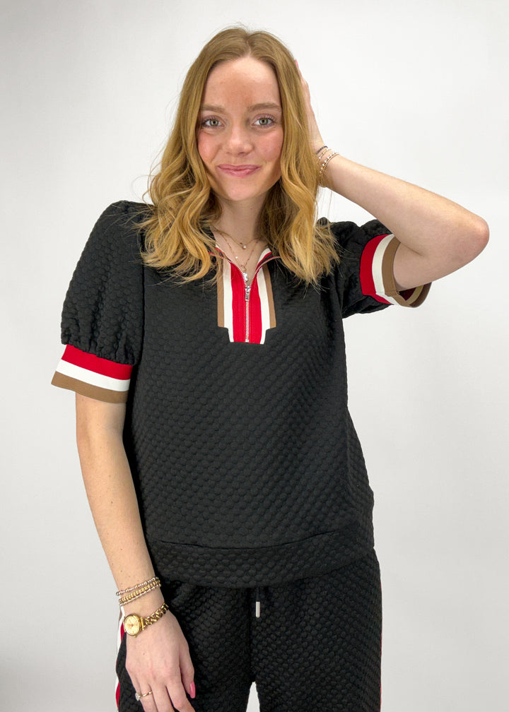 Woman wearing a black textured outfit with red and white accents on a plain background