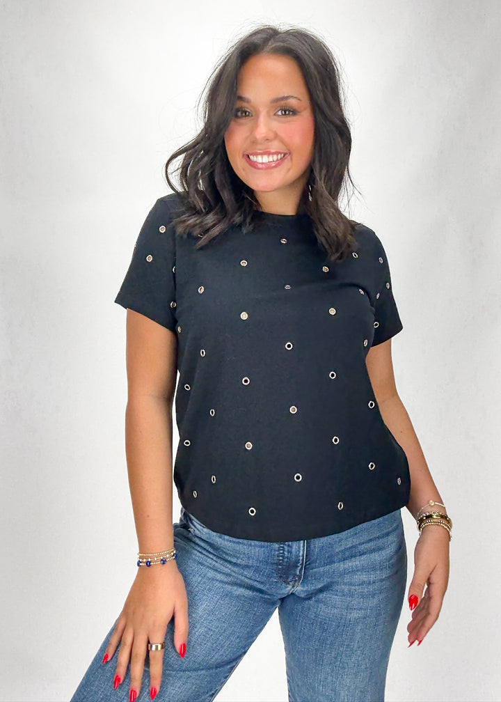 Woman wearing a black top with silver embellishments and blue jeans on a white background