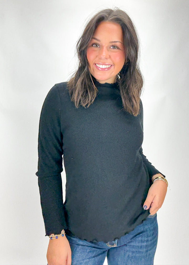 Woman wearing a black turtleneck sweater and blue jeans against a white background