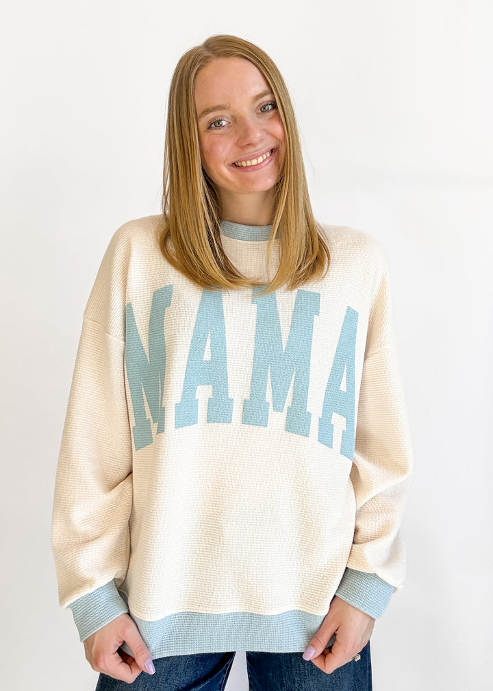 Person wearing a cream sweater with 'MAMA' printed in blue on a plain background