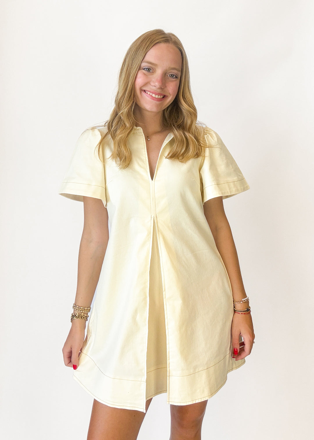 Woman wearing a cream dress with front pleats on a white background